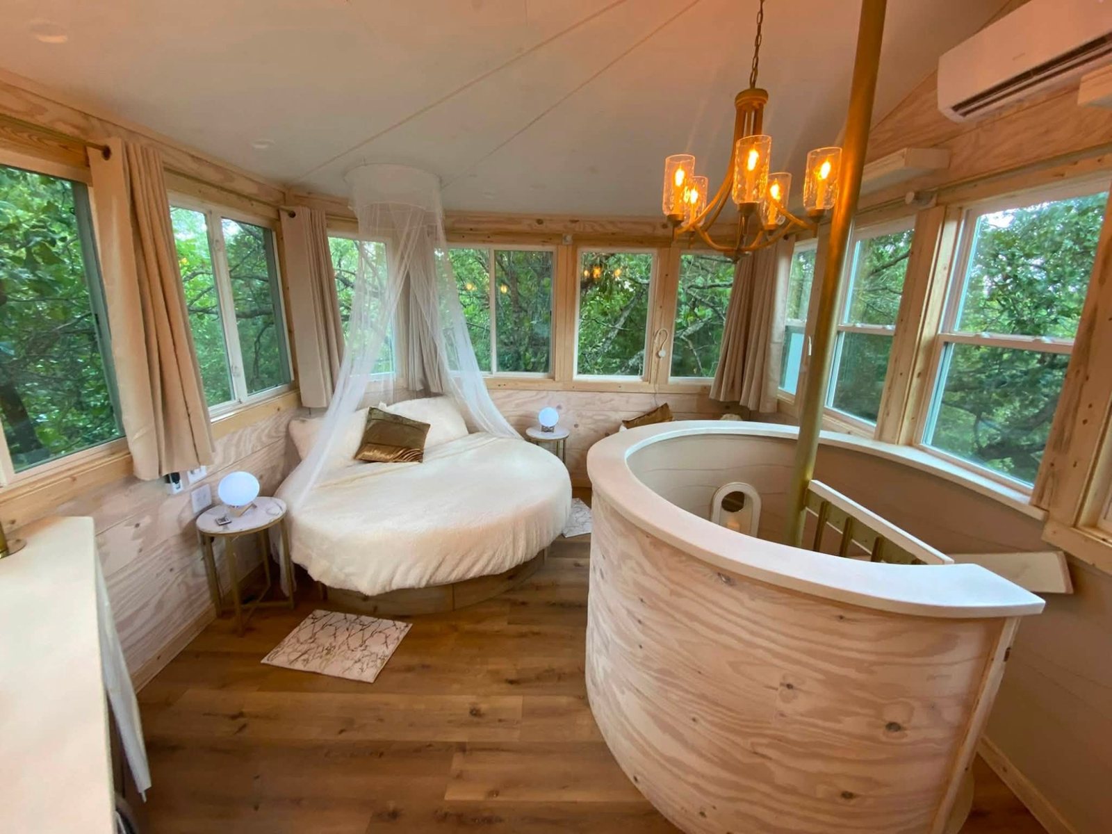 Round canopy bed under a candle chandelier, ringed by treetop windows
